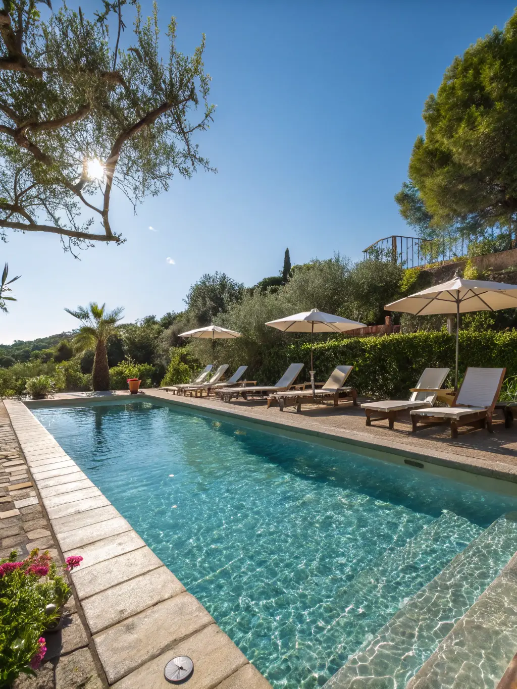 A beautifully landscaped communal garden in Can Bruguera, featuring lush greenery, a swimming pool, and comfortable lounge chairs, creating a relaxing and inviting outdoor space for residents.